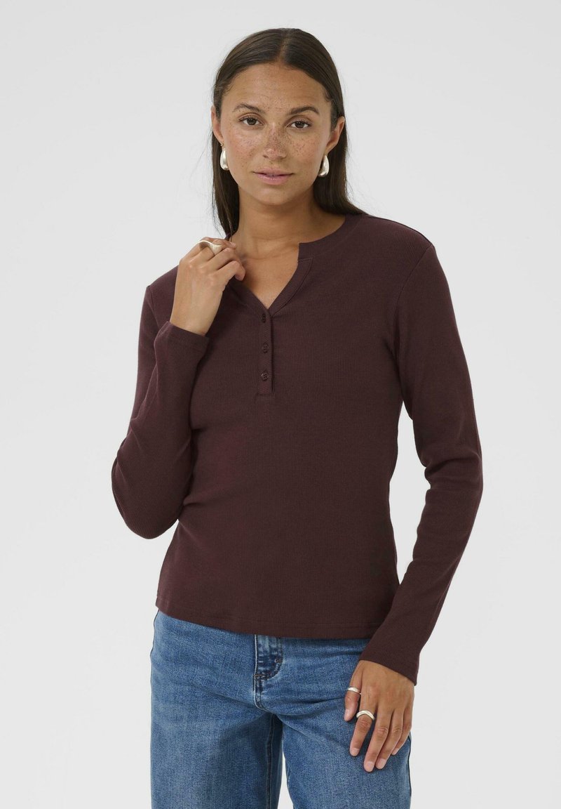 Burgundowa longsleeve koszulka henley z okrągłym dekoltem, trzema guzikami oraz prążkowaną teksturą, w połączeniu z niebieskimi dżinsami.