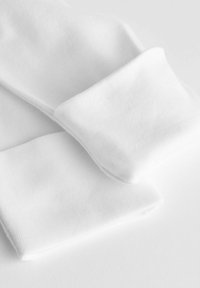 Chaussettes blanches en coton présentant une texture lisse avec des bords roulés, posées à plat sur un fond blanc.