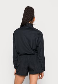 Top negro de cuello alto y manga larga combinado con pantalones cortos negros. El top tiene un ajuste holgado y puños elásticos; los pantalones cortos cuentan con una tela texturizada.