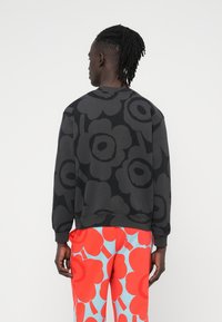 Μαύρο φούτερ με μεγάλο σκούρο λουλουδάτο σχέδιο, στρογγυλή λαιμόκοψη και μακριά μανίκια. Συνδυασμένο με κόκκινο και ανοιχτό μπλε παντελόνι με σχέδιο.