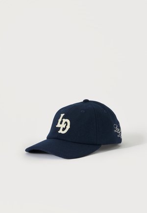 Casquette de baseball bleu marine avec des lettres stylisées blanches brodées "LD" à l'avant et un texte en cursive sur le côté, affichée sur fond blanc.