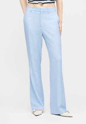 Žena v svetlomodrých širokých vysoký pás nohaviciach s vreckami, doplnených o biele špicaté baleríny a pruhovaný orezaný top.