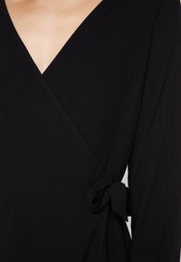 Robe noire à encolure en V plongeante, manches longues et ceinture nouée à la taille. Fabriquée en tissu lisse et léger.