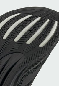 Suola della scarpa in gomma nera con strisce bianche. Presenta un battistrada testurizzato per la presa e curvature per la flessibilità, evidenziando un design funzionale.