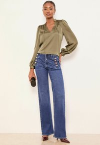 Satiinist oliivroheline pluus puffvarrukatega, kombineeritud kõrge vöökohaga siniste teksadega, millel on kuldsed nööpdetailid.