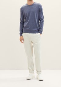 Niebieski sweter w serek z miękkiej dzianiny, zestawiony z jasnobeżowymi spodniami i białymi trampkami, charakteryzujący się luźnym krojem i mankietami.