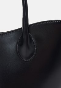 Sort læder håndtaske med glat overflade, afrundede håndtag og synlige syninger omkring bunden og punkterne for håndtagets fastgørelse.