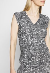 Robe à motifs noir et blanc avec un col en V, des courtes manches gigot, une taille ajustée, et un dessin complexe de fleurs et de spirales partout.