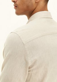Lichtbeige overhemd van gestructureerde stof met een kraag. Kenmerkt zich door een achterpand en subtiele stikdetails op de mouwen.