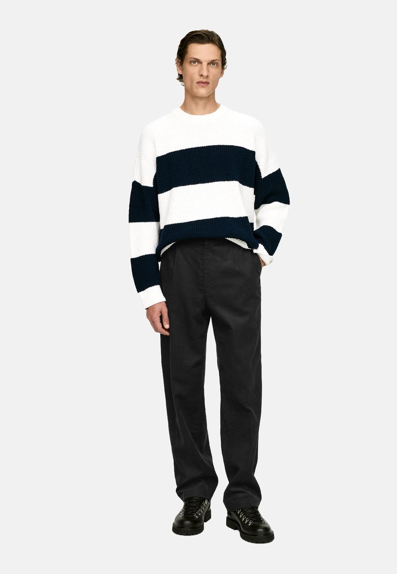 Pull en maille rayé bleu marine et blanc, associé à un pantalon noir. Le pull présente une coupe décontractée et un tissu texturé. Des chaussures noires à lacets complètent le look.
