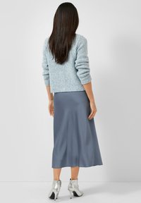 Lichtblauwe gebreide trui met geribbelde manchetten en zoom, gecombineerd met een grijze, vloeiende mid-length rok en metallic enkelhoge laarzen.