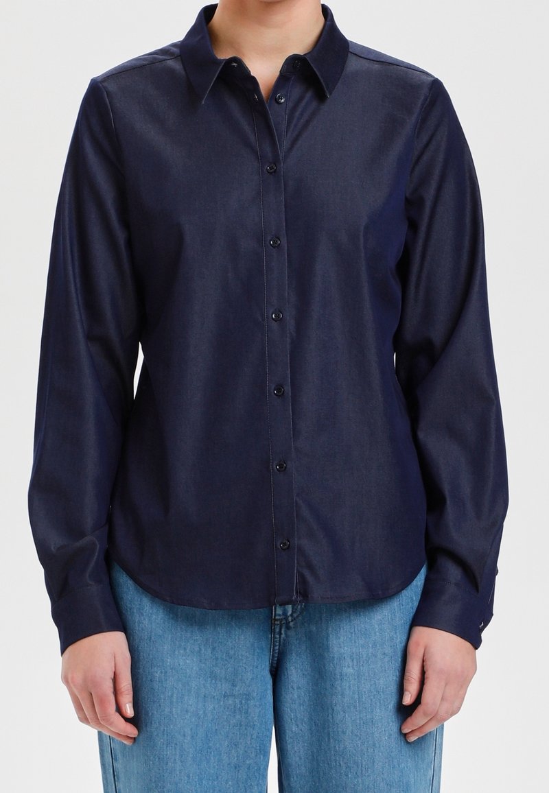 Camisa navy de botones con tejido suave, de manga larga, cuello clásico y dobladillo curvado, combinada con unos pantalones de mezclilla azul claro.