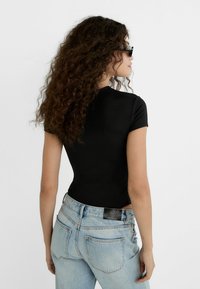 Schwarzer, figurbetonter, kurzärmliger Body, kombiniert mit hellblauen, hochbundigen Jeans, die ein Lederetikett auf der Rückseite und eine glatte Textur aufweisen.