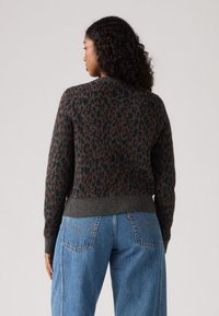 Suéter cinza tricotado com um padrão de leopardo laranja e preto, apresentando um decote redondo e bainha canelada, combinado com jeans de perna larga azul.