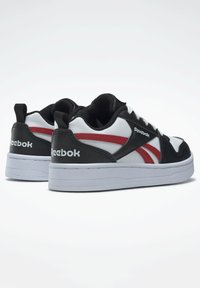 Baskets noires et blanches avec des accents rouges, featuring un dessus en cuir lisse, un col rembourré et une semelle en caoutchouc blanc. Logo Reebok affiché.
