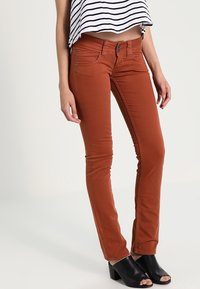 Ruskvärgade, figursydda jeans med en slät textur, som har en klassisk femficksdesign, dubbelknäppning och minimala söm detaljer.