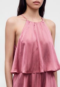 Femme portant un haut dos nu rose en satin avec des bretelles fines et une coupe ample et fluide.