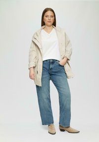 Lichtbeige jas, witte v-hals shirt, lichtblauwe wijde jeans en beige enkellaarsjes. Glad materiaal, ontspannen pasvorm, eenvoudig ontwerp.