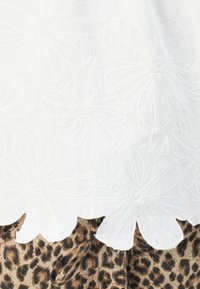 Tissu blanc brodé avec de grands motifs floraux au bas, présenté au-dessus d'un textile à imprimé léopard.