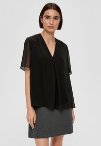Schwarze Bluse mit kurzen Ärmeln, V-Ausschnitt und fließendem Design, kombiniert mit einem schmalen grauen Rock. Glatte Textur und leichtes Material.