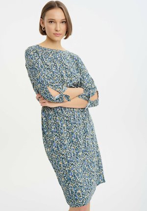 Vestido floral en tonos azules y amarillos, con un corte relajado, mangas tres cuartos con detalles de lazo y largo hasta la rodilla.