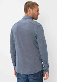 Herren Langarmhemd aus strukturiertem blauen Stoff mit Kragen, Rückenpasse und geknöpften Manschetten. Verfügt über einen geschwungenen Saum und ein dezentes Muster.