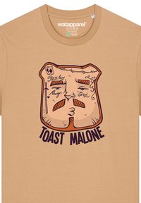 Beige t-shirt gemaakt van katoen, met een cartoonachtige toastfiguur met gestileerde gezichtskenmerken en de tekst "TOAST MALONE" in vetgedrukte, donkere letters.
