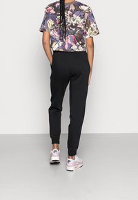 Cropped floral-patterned shirt in various colors, paired with black sweatpants and white-pink Nike sneakers, emphasizing relaxed style.