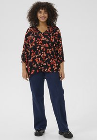 Blusa negra con estampado floral rojo, escote en V y mangas de tres cuartos. Combinada con jeans de pierna ancha azules y zapatos de plataforma negros.