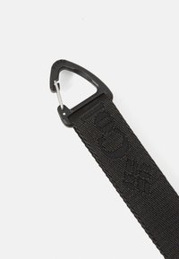 Sorte nylonrem med en særpræget vævet tekstur og en metalkarabinlås til fastgørelse. Præget mønster synligt på remmen.