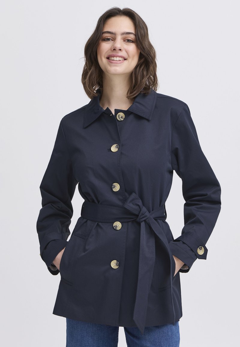 Marineblauer Trenchcoat mit tailliertem Gürtel, großen goldenen Knöpfen und seitlichen Taschen. Leichter Stoff und ein Kragen.