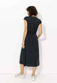 Robe noire midi à manches courtes, taille froncée, en tissu léger et texture lisse, portée avec des baskets argentées.