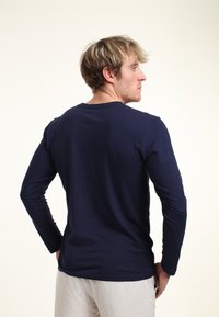 Mörkblå långärmad skjorta i lätt tyg, med rundad halsringning och utan sömmar på baksidan. Bärs tillsammans med ljusa byxor.