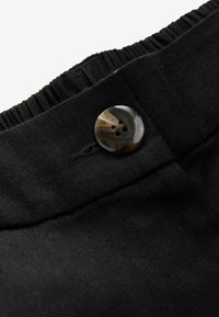 Ceinture en tissu noir avec un élastique froncé et un bouton marbré à quatre trous, détail de couture le long du bord, et une texture lisse.