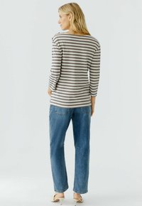 Gestreift, langärmliges Oberteil in Grau und Weiß, mit einem weiten Ausschnitt und Knopfdetails. Kombiniert mit hellblauen, geraden Jeans.
