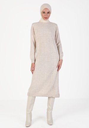 Beige knitted dress with ribbed texture, long sleeves, and a high neckline. Paired with tall, light-colored boots.