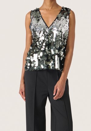 Ärmelloses V-Ausschnitt-Oberteil, bedeckt mit großen silbernen Pailletten, kombiniert mit hoch taillierten schwarzen Hosen mit weitem Bein, getragen von einer stehenden Person.