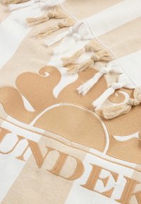 Tessuto con strisce alternate beige e bianche, caratterizzato da un grande e intricato motivo beige e frange lungo un bordo, enfatizzato dalla texture.