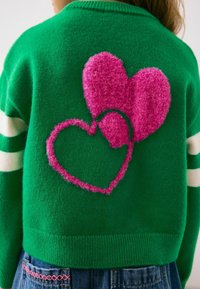 Green knit sweater with pink fluffy heart designs on the back, featuring white striped sleeves and a ribbed hem.