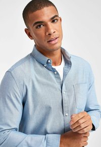 Himmelblaues Button-up-Hemd mit einer Brusttasche und einer weichen Textur. Der Kragen ist heruntergeklappt, und das Hemd hat ein Design mit einem einzelnen Manschette.