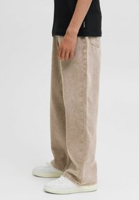 Bež kavbojke širokega kroja z zbledelim videzom, z nastavljivimi zankami in zadnjimi žepi. V kombinaciji z belimi supergami za kontrast.