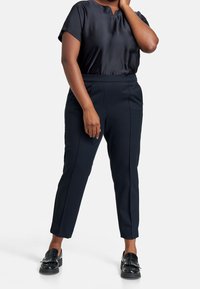 Zwart satijnen top met korte mouwen, gecombineerd met een op maat gemaakte marineblauwe broek. De broek heeft een aansluitende taille en rechte pijpen. Zwarte loafers maken de look af.