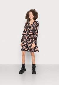 Vestido preto com estampado floral e mangas longas, apresentando flores rosas e laranjas, e uma bainha ampla. Combinado com botas de combate pretas.