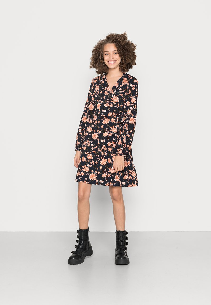 Vestido preto com estampado floral e mangas longas, apresentando flores rosas e laranjas, e uma bainha ampla. Combinado com botas de combate pretas.