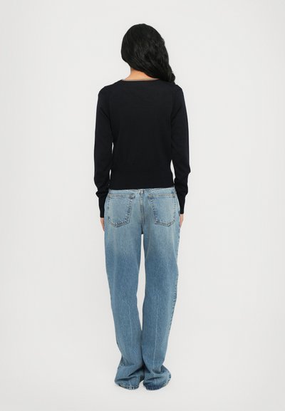 Maglione blu navy con scollo a girocollo, maniche lunghe e orlo a coste abbinato a jeans a vita alta di un leggero blu e dal fitting rilassato.