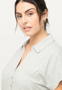 Camisa gris de manga corta con cuello, con un cierre frontal de botones y una tela texturizada sutil.