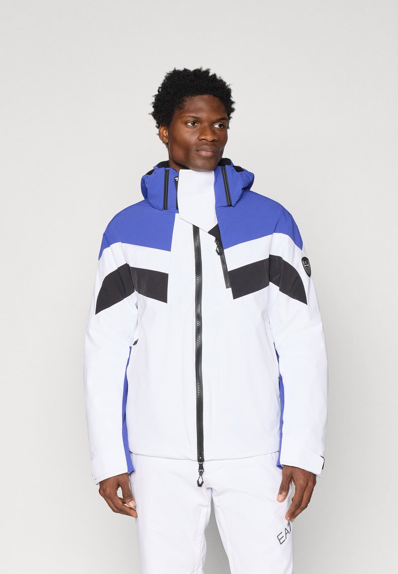 Meeste jope, mis on valmistatud veekindlast materjalist, sinise, valge ja musta värviblokiga disainiga, kõrge kraega ja esise luku sulgemisega.