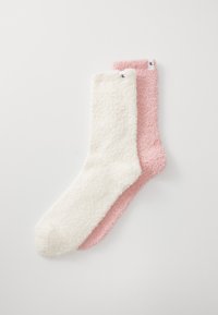 Um par de meias felpudas, uma em creme e a outra em rosa claro. Cada uma apresenta uma textura macia e uma pequena etiqueta da marca na bainha.
