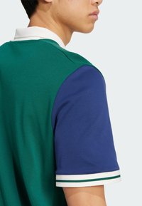 Green and blue color-blocked polo shirt with a white collar, featuring striped accents on the sleeves and a textured fabric.