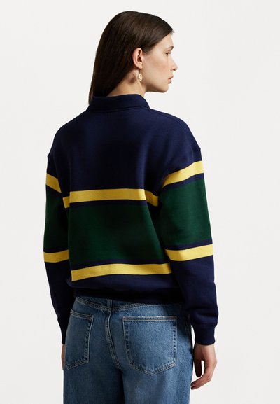 Navy blue sweatshirt with green and yellow horizontal stripes, featuring a relaxed fit and collared neckline. Worn with light blue jeans.